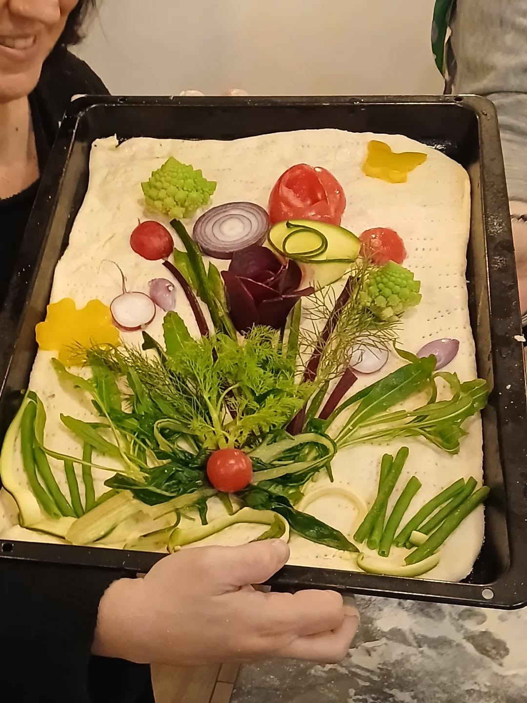 Focaccia cruda in teglia decorata con un bouquet di verdure: pomodorini, cipolla rossa, romanesco, fagiolini e finocchietto